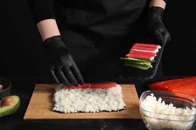 Photo of Chef in gloves making sushi roll at dark table, closeup