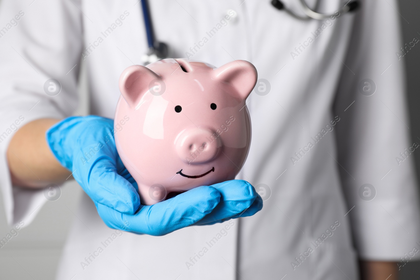 Photo of Doctor holding pale pink ceramic piggy bank, closeup. Medical insurance