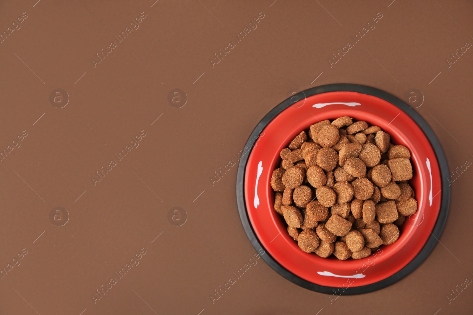 Photo of Dry dog food in feeding bowl on brown background, top view. Space for text