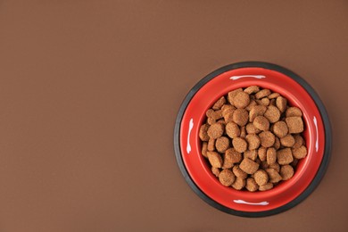 Photo of Dry dog food in feeding bowl on brown background, top view. Space for text