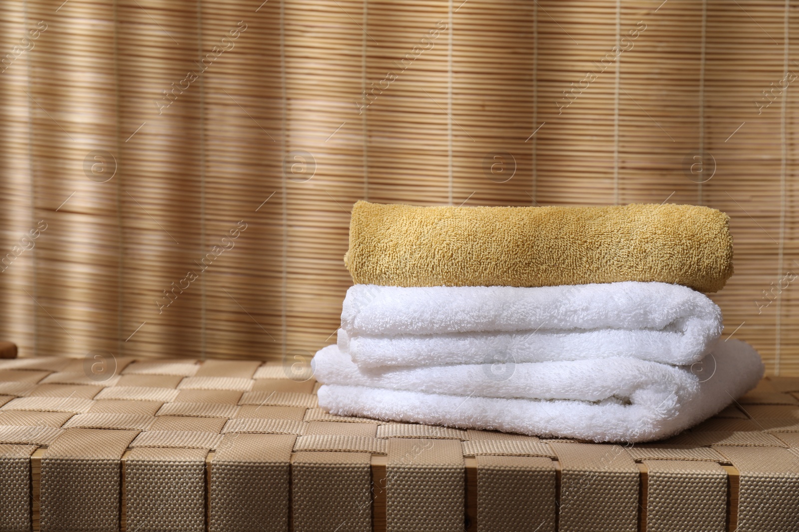 Photo of Stacked soft towels on wicker bench indoors, space for text