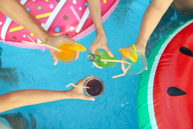 Photo of People toasting with refreshing drinks at pool party, top view