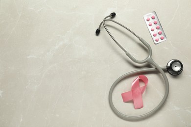 Breast cancer awareness. Pink ribbon, stethoscope and pills on light grey table, flat lay. Space for text