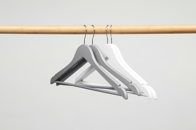 Photo of Empty clothes hangers on wooden rail against light background