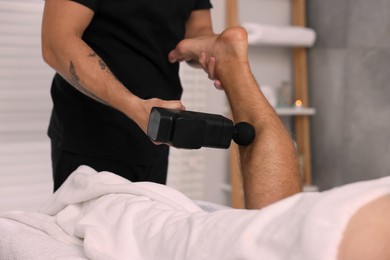 Photo of Man receiving professional leg massage with electric gun in spa salon, closeup