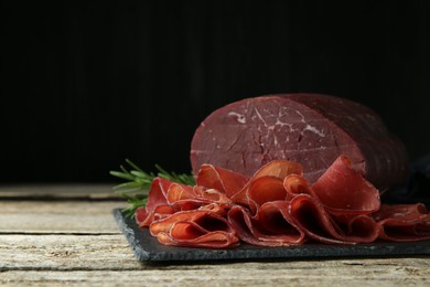 Photo of Tasty bresaola and rosemary on wooden table, closeup