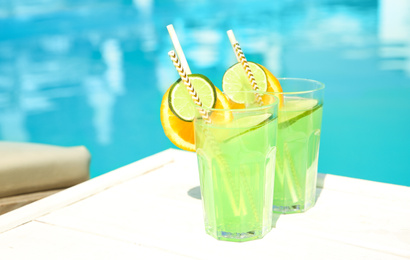 Refreshing cocktail in glasses near outdoor swimming pool on sunny day. Space for text