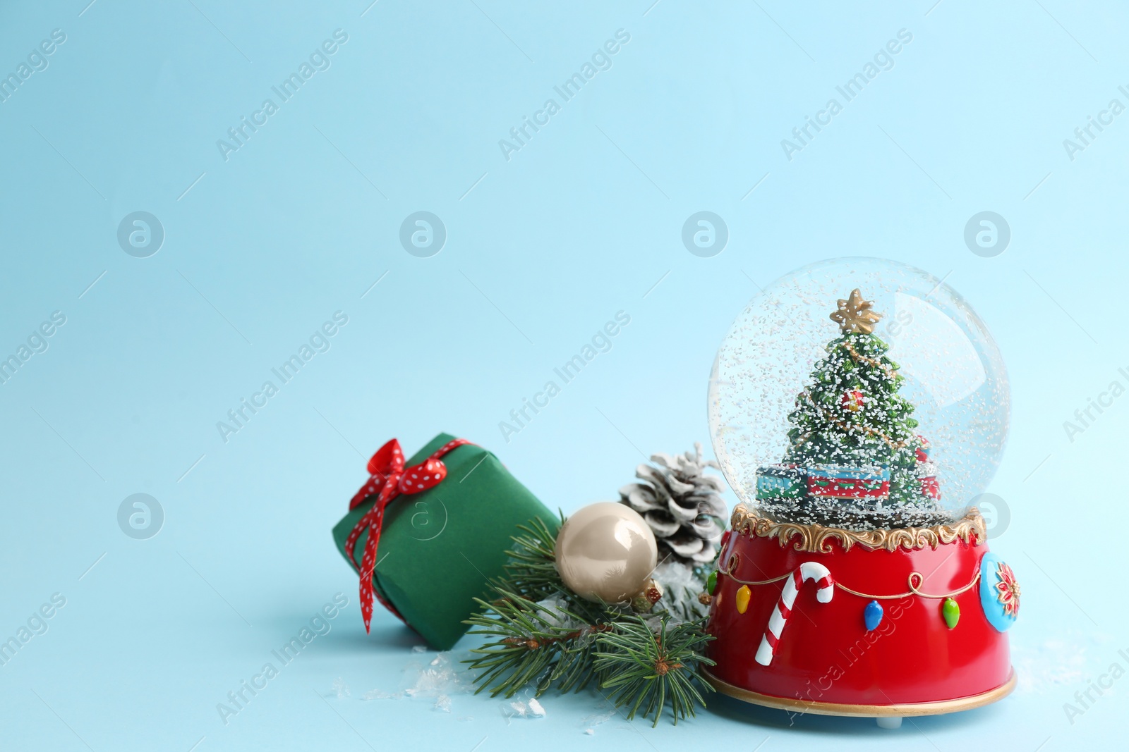 Photo of Beautiful snow globe and Christmas decor on light blue background, space for text