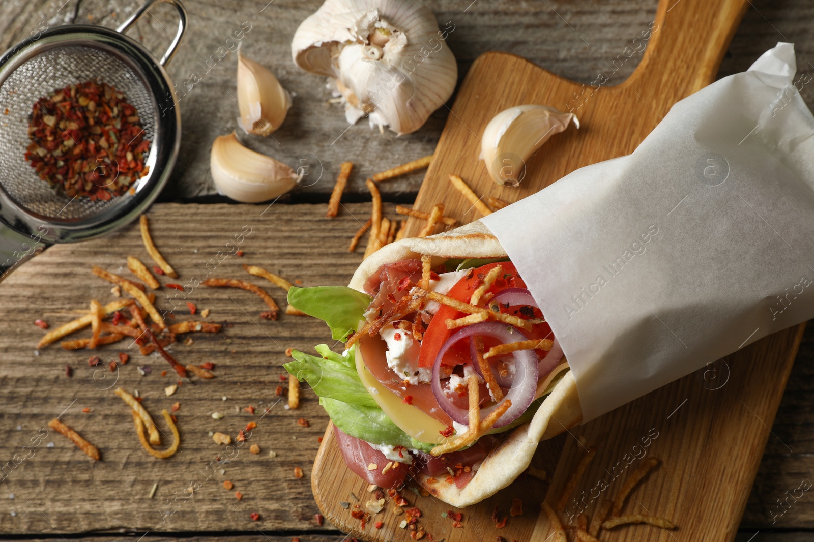 Photo of Delicious pita wrap with prosciutto and vegetables on wooden table, flat lay. Space for text