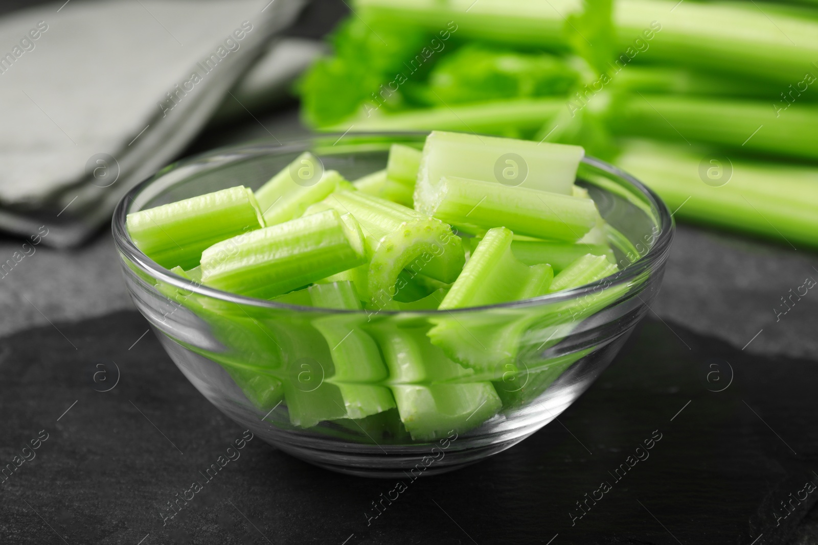 Photo of Bowl with fresh green cut celery on grey table, closeup