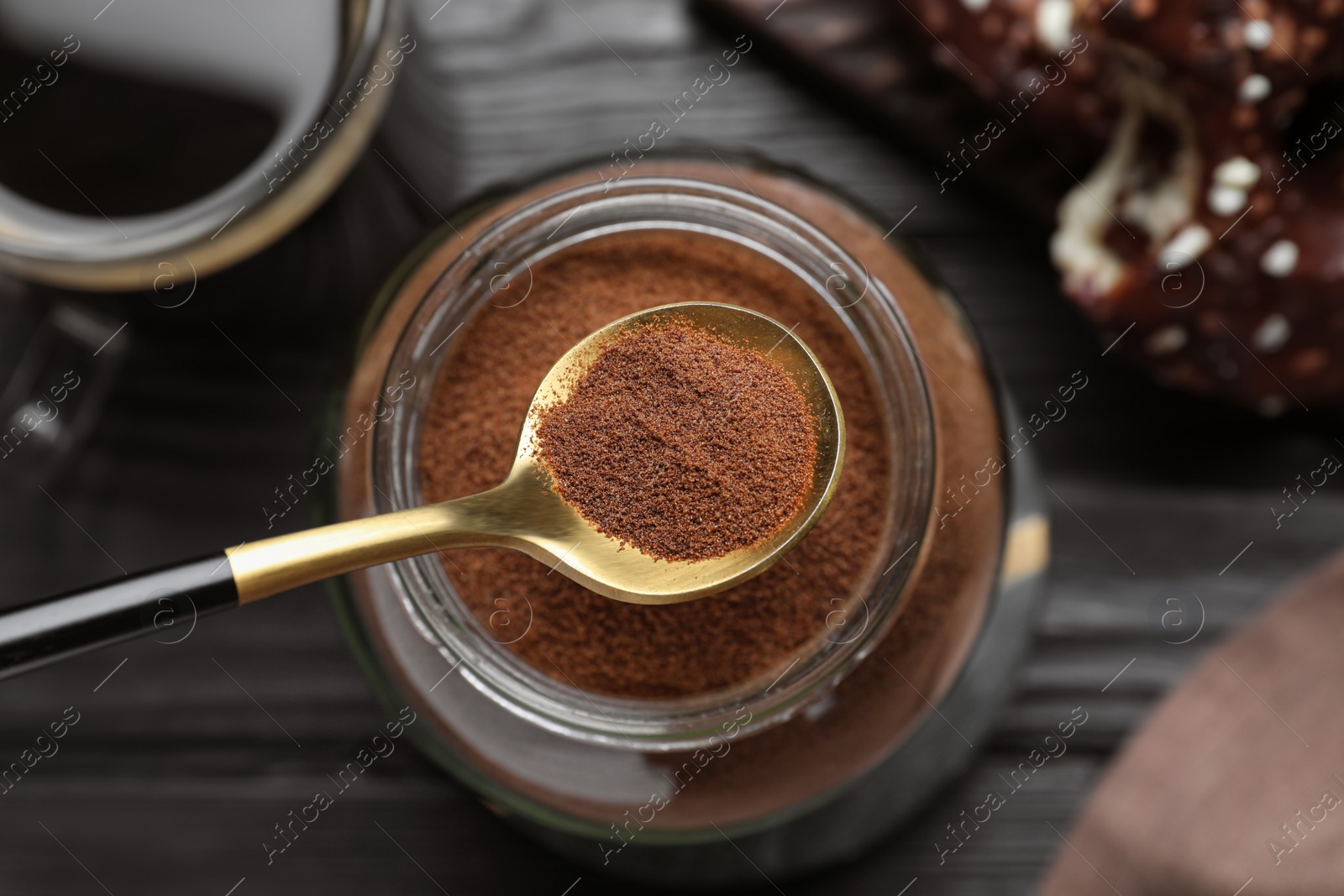 Photo of Spoon of instant coffee over jar on black wooden table, top view