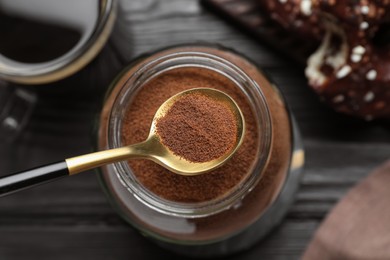 Spoon of instant coffee over jar on black wooden table, top view