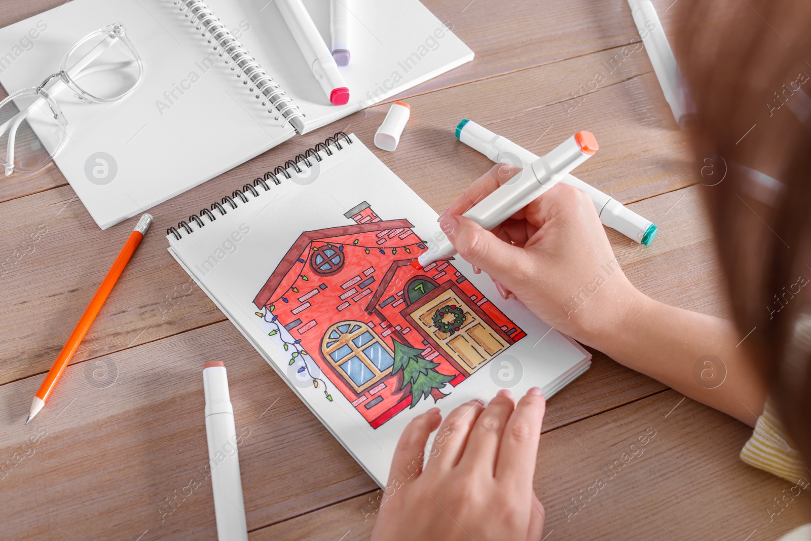 Photo of Woman drawing in sketchbook with felt tip pen at wooden table, closeup