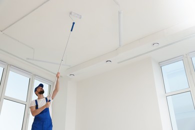 Photo of Worker in uniform painting ceiling with roller indoors. Space for text
