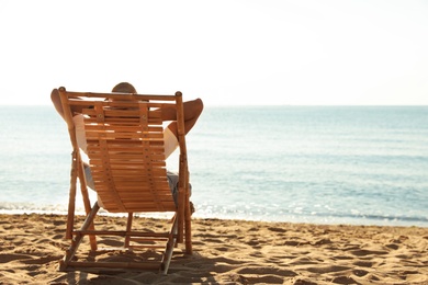 Photo of Man relaxing on deck chair at sandy beach. Summer vacation