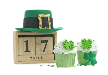 Photo of St. Patrick's day, party on 17th of March. Tasty festively decorated cupcakes, green leprechaun hat and wooden block calendar, isolated on white