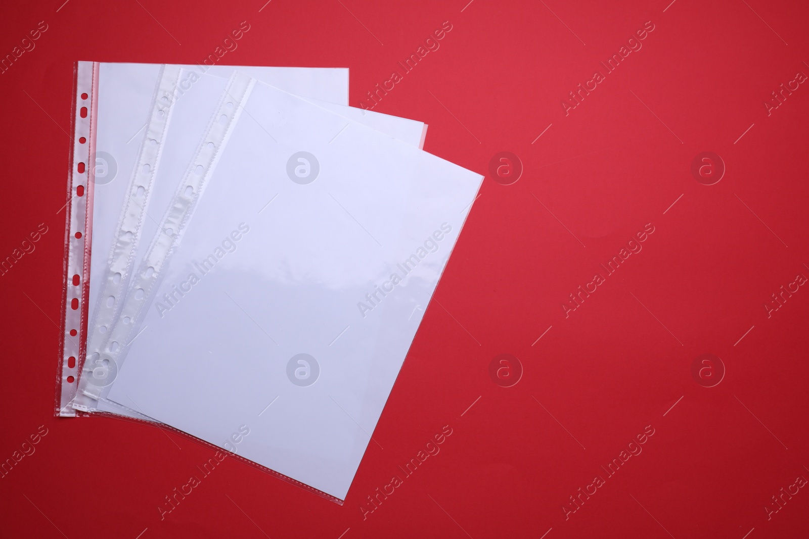 Photo of Punched pockets with paper sheets on red background, flat lay. Space for text