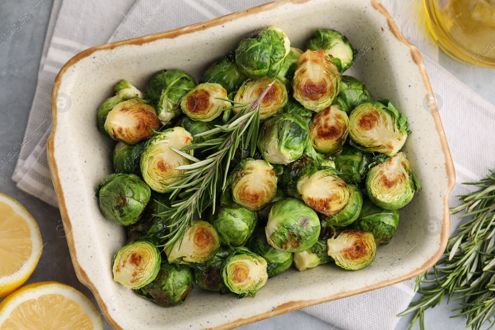 Photo of Delicious roasted Brussels sprouts, rosemary and lemon on grey table, top view