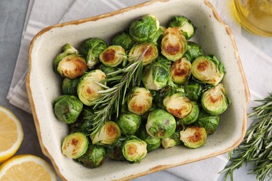 Delicious roasted Brussels sprouts, rosemary and lemon on grey table, top view