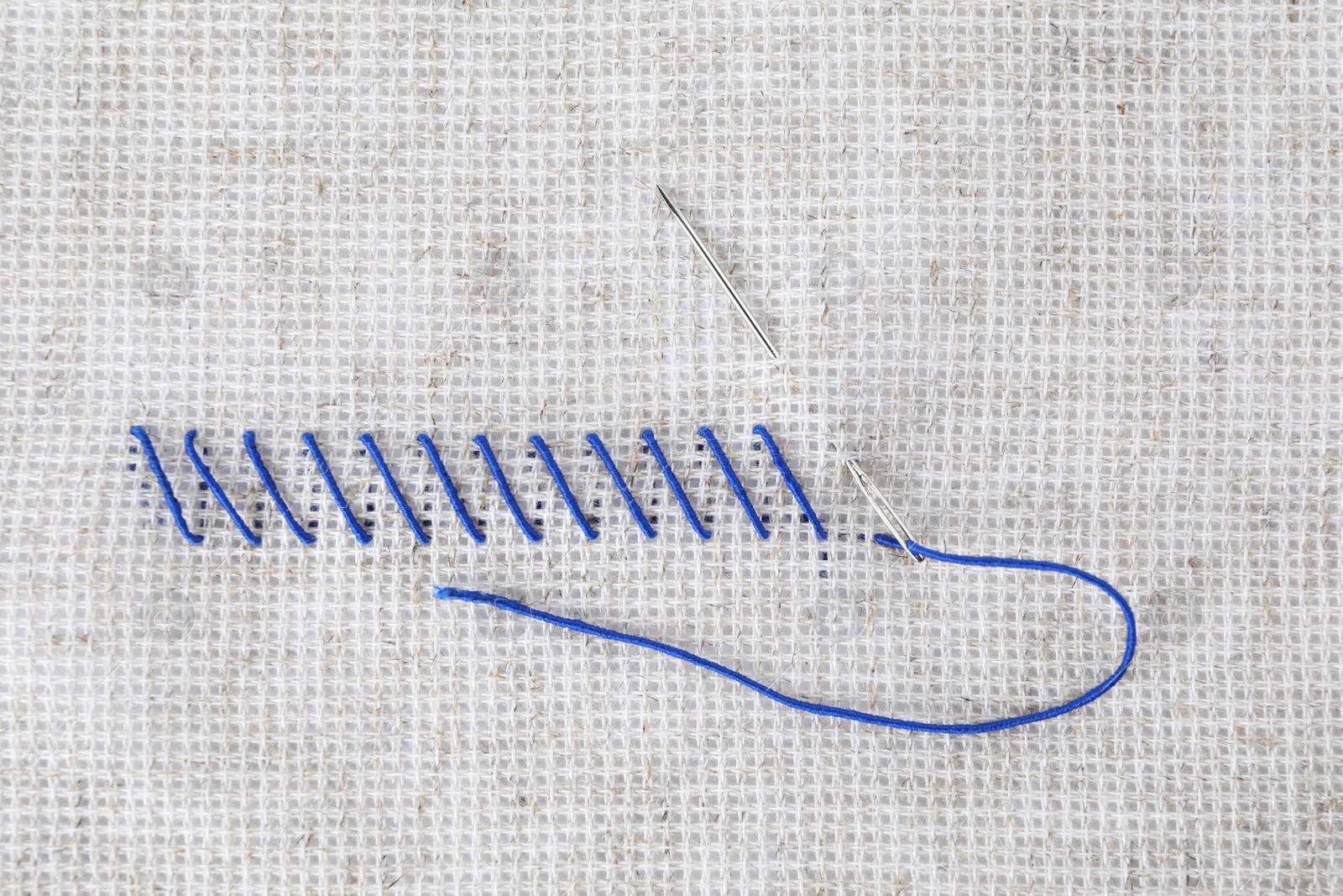 Photo of Canvas with blue embroidery and needle, top view