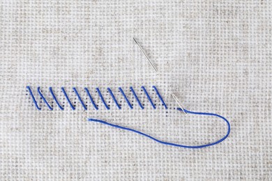 Photo of Canvas with blue embroidery and needle, top view