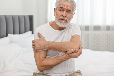 Arthritis symptoms. Man suffering from pain in elbow on bed at home