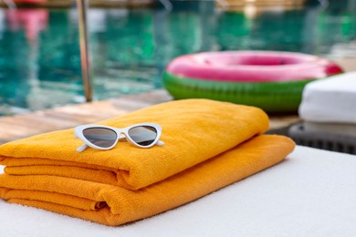 Beach towels and sunglasses on sun lounger near outdoor swimming pool. Luxury resort