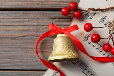 Photo of Golden shiny bell with red bow, music sheets and decorative branch on wooden table, flat lay. Space for text. Christmas decoration