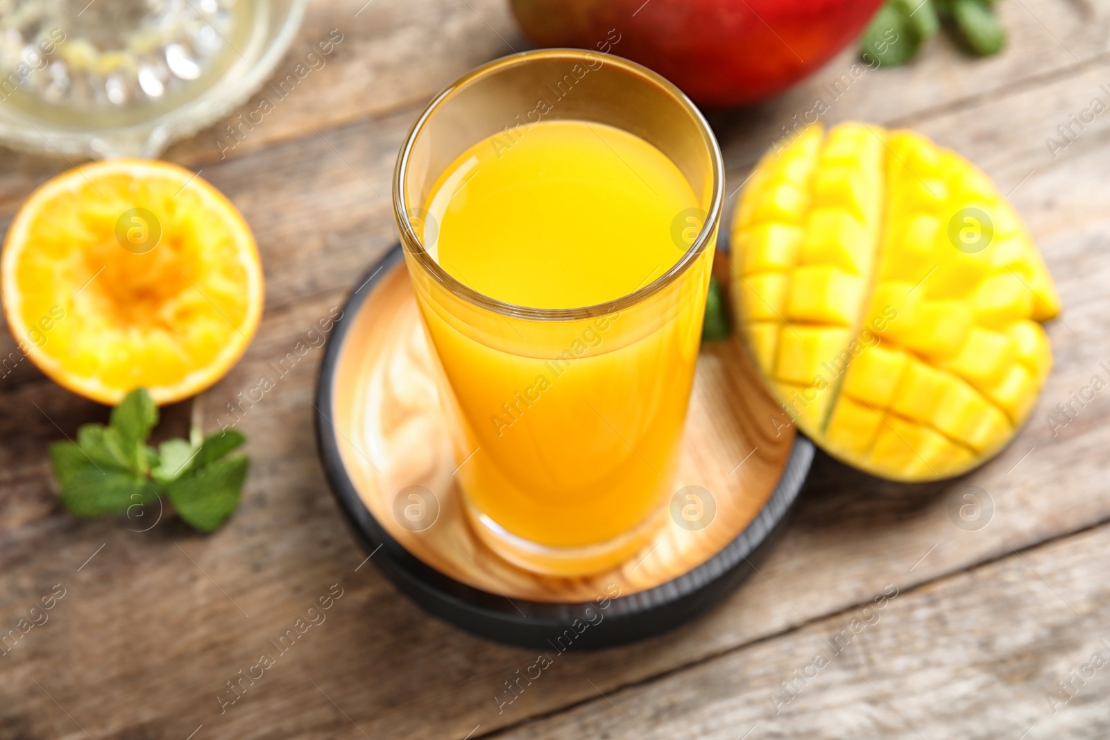 Photo of Glass of fresh mango drink and tropical fruits on wooden table