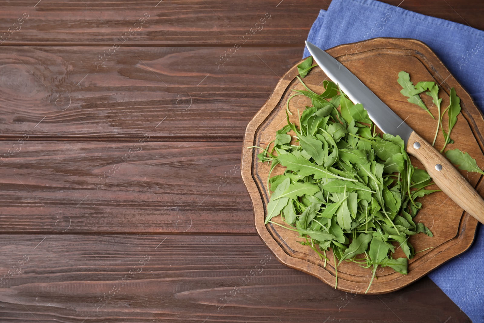 Photo of Cutting board with fresh arugula leaves and knife on wooden table, flat lay. Space for text