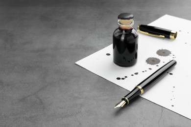 Photo of Stylish fountain pen, bottle and paper with blots of ink on grey textured table, space for text