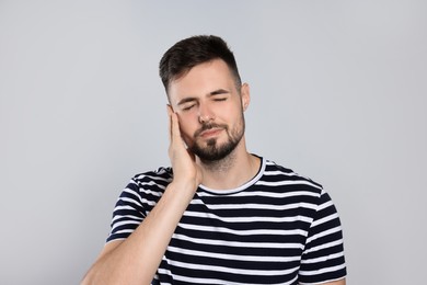 Young man suffering from ear pain on light grey background