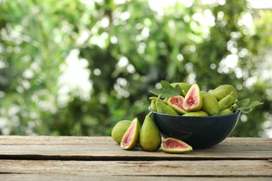 Cut and whole green figs on wooden table against blurred background, space for text