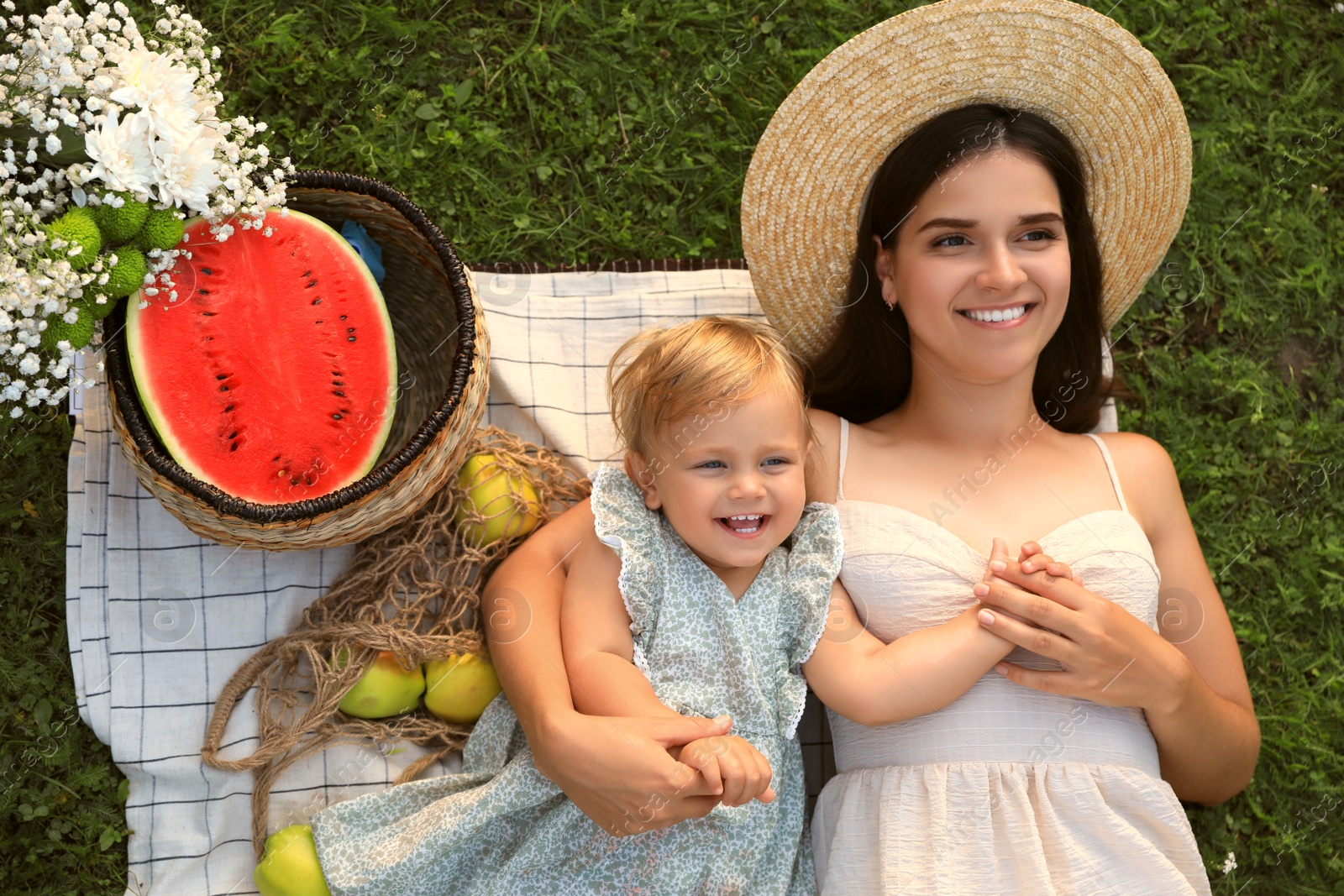 Photo of Mother and her baby daughter resting while having picnic on green grass outdoors, top view