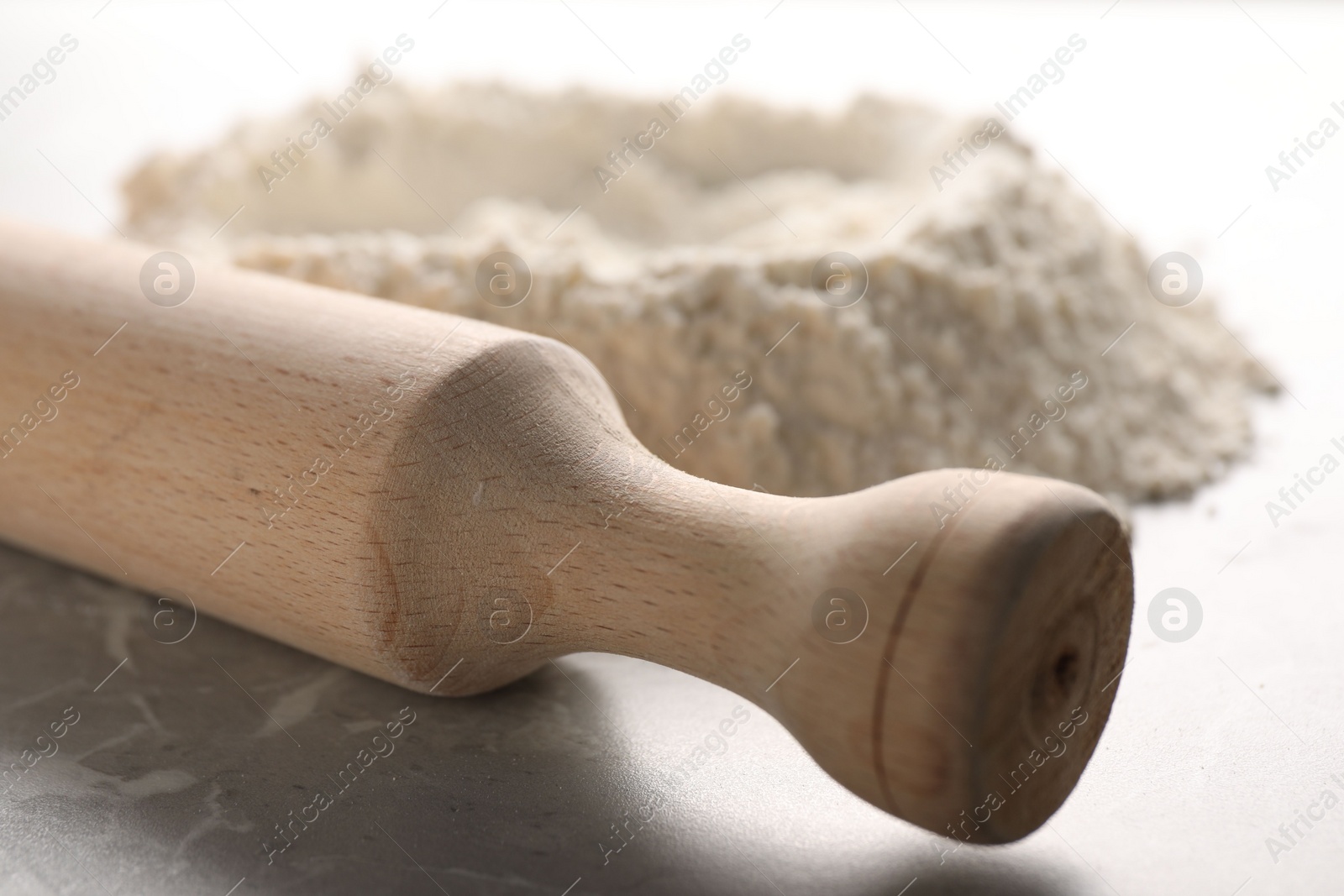 Photo of Rolling pin and flour on grey marble table, closeup