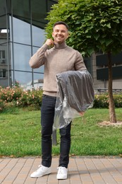 Man holding garment cover with clothes outdoors. Dry-cleaning service