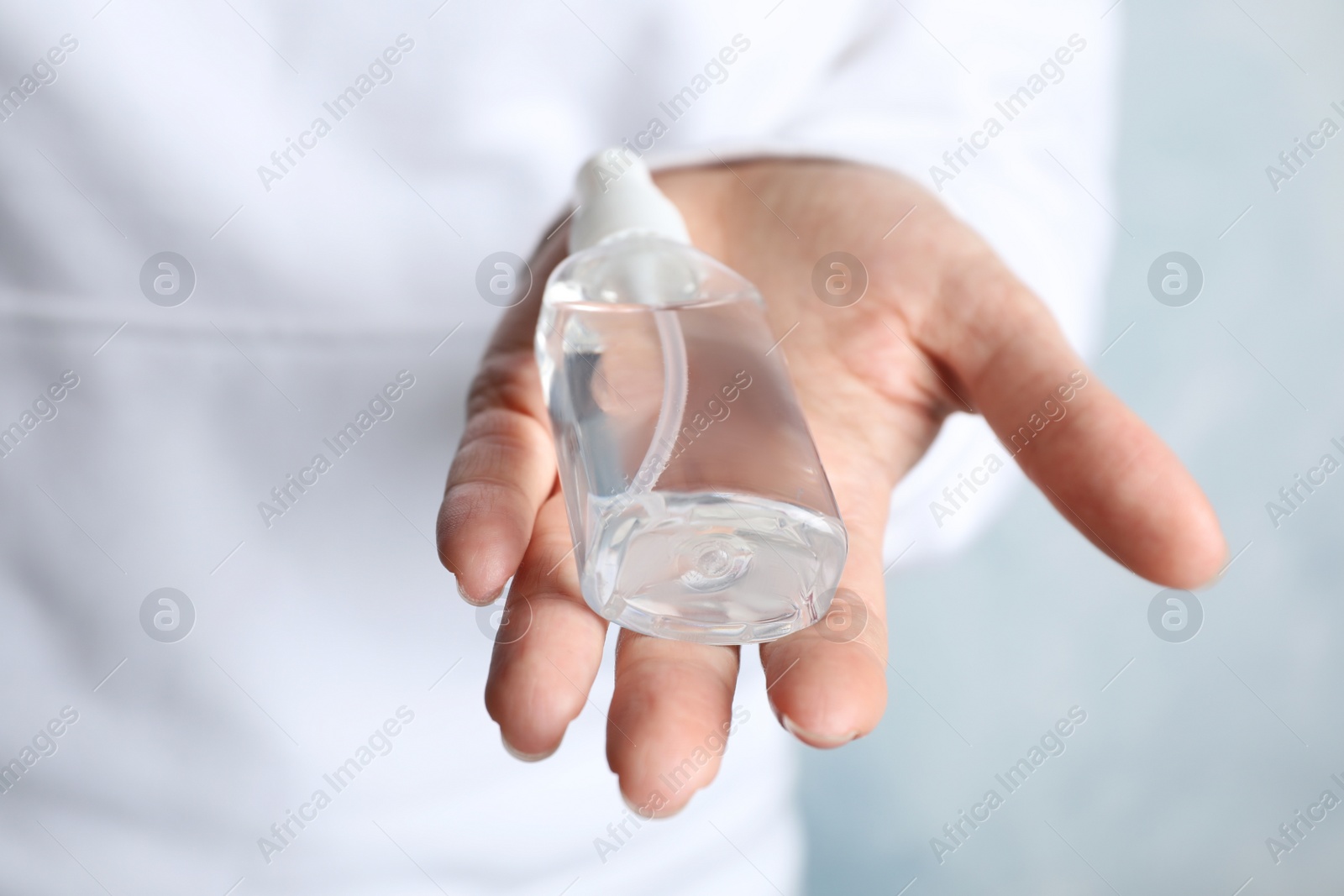 Photo of Woman holding antiseptic spray on light background, closeup