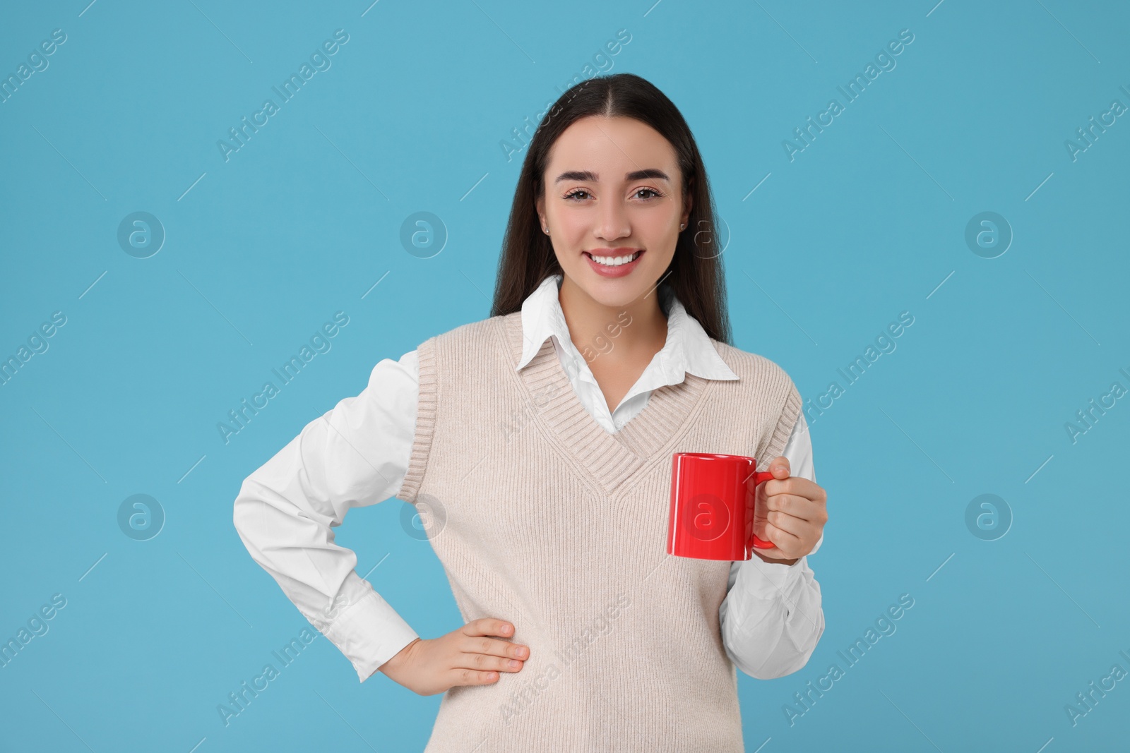 Photo of Happy young woman holding red ceramic mug on light blue background