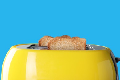 Photo of Modern toaster with slices of roasted bread against light blue background, closeup