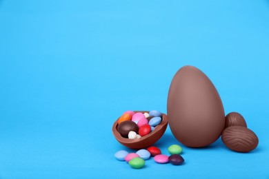 Photo of Delicious chocolate eggs and candies on light blue background. Space for text