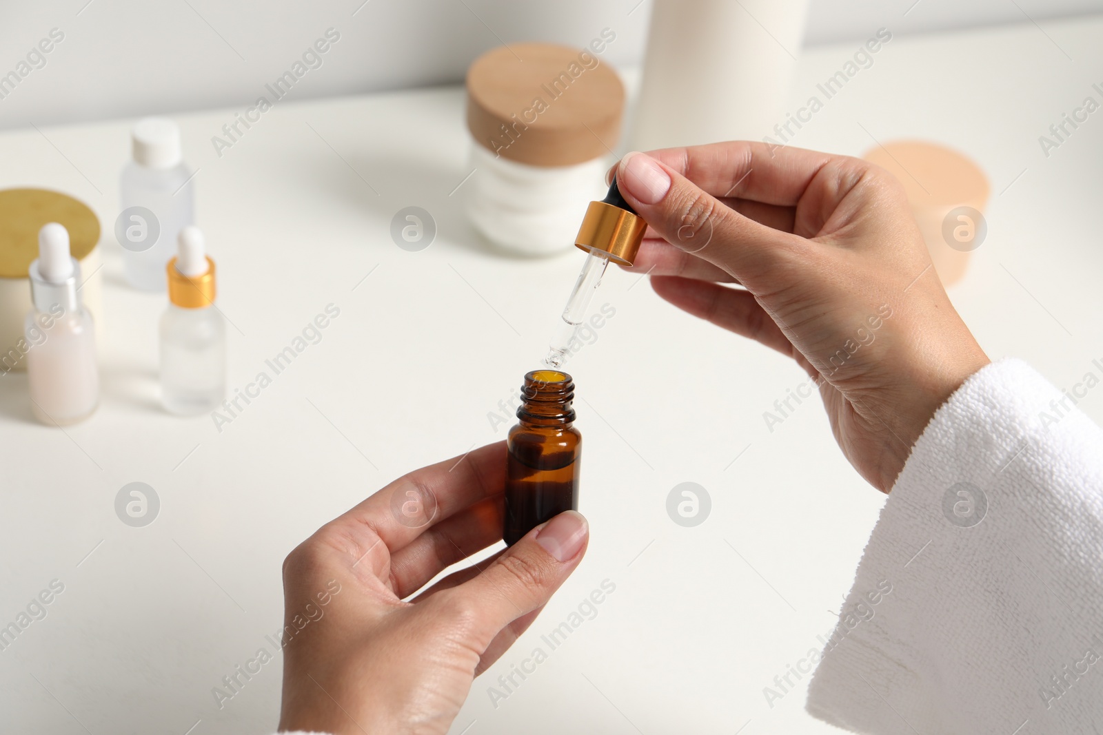 Photo of Woman with bottle of cosmetic serum and pipette at white table, closeup