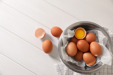 Photo of Fresh raw chicken eggs with bowl on white wooden table, flat lay. Space for text