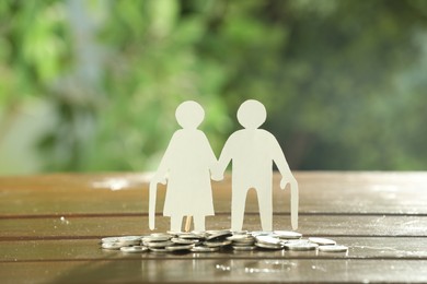 Pension savings. Figure of senior couple and coins on wooden table outdoors