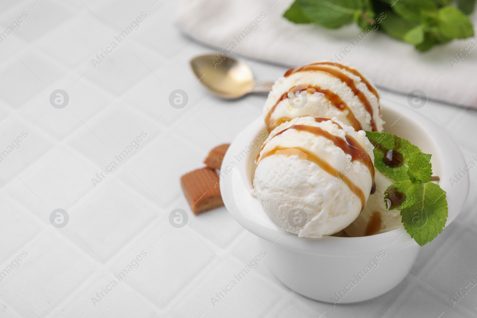 Photo of Scoops of tasty ice cream with mint and caramel sauce on white tiled table, space for text
