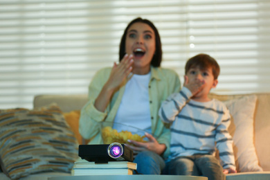 Photo of Young woman and her son watching movie at home, focus on video projector