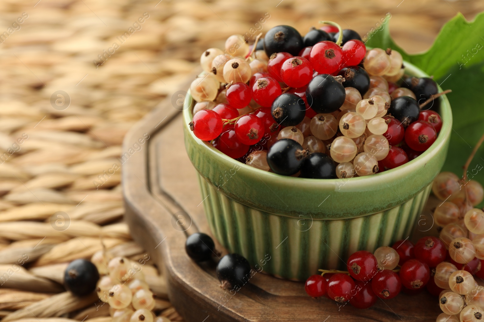 Photo of Different fresh ripe currants on wicker surface, closeup. Space for text