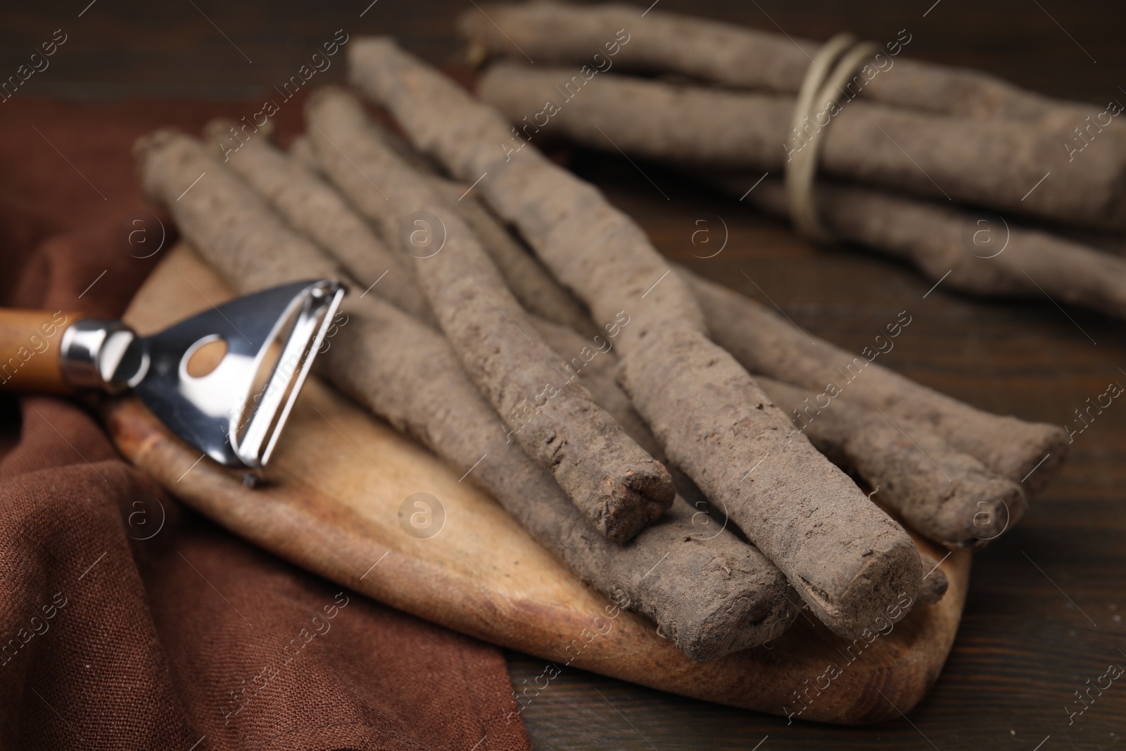 Photo of Raw salsify roots and peeler on wooden table, closeup