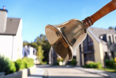 Image of Golden school bell with wooden handle and blurred view of street on sunny day