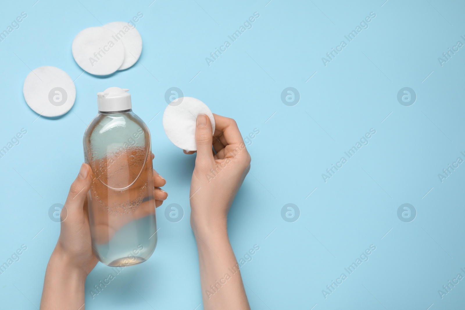 Photo of Woman holding makeup remover and cotton pad on light blue background, top view. Space for text