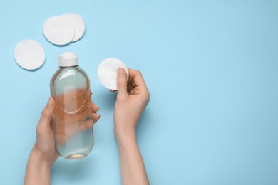 Woman holding makeup remover and cotton pad on light blue background, top view. Space for text